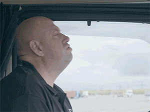 Bald man at the wheel of a truck leans his head down on the wheel in exhaustion.