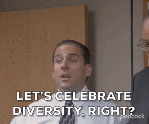 Michael Scott in a white button up shirt and a black and grey tie crosses his arms in an office meeting room and says, "Let's Celebrate Diversity, right?"
