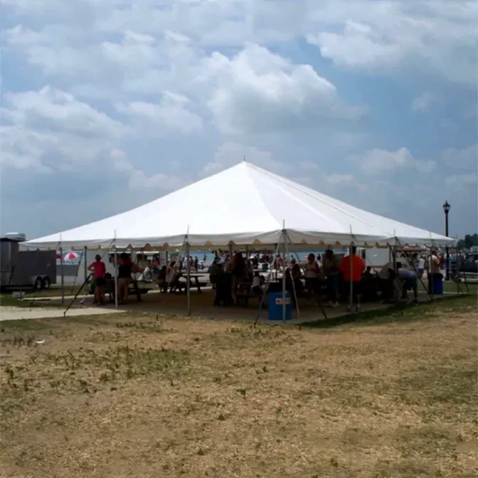 Large white tent at an outdoor event with people seated beneath, surrounded by grass and overcast sky.