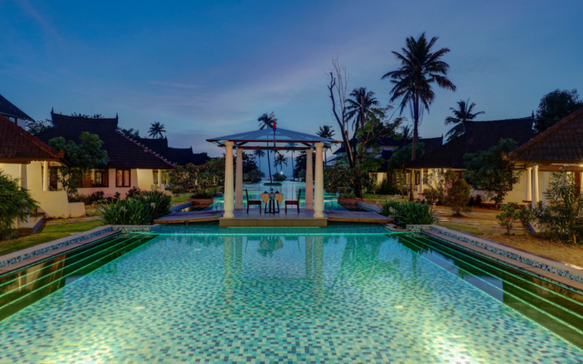 Elegant Sri Lankan beachfront wellness resort at twilight featuring a serene central swimming pool, tropical villas, palm trees, and oceanfront relaxation.