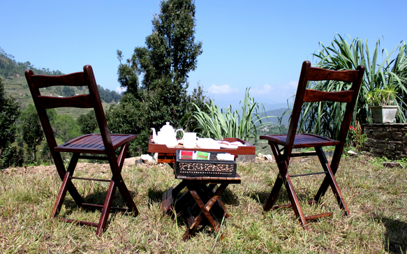 Outdoor tea setup with wooden chairs and table overlooking a scenic mountain landscape