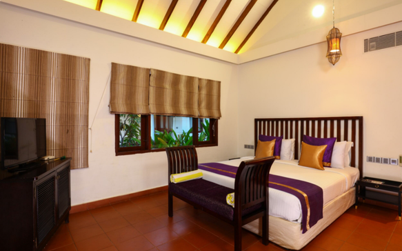 Warm and inviting Sri Lankan Ayurvedic retreat bedroom featuring traditional wood furnishings, high ceilings, and serene wellness accommodation.