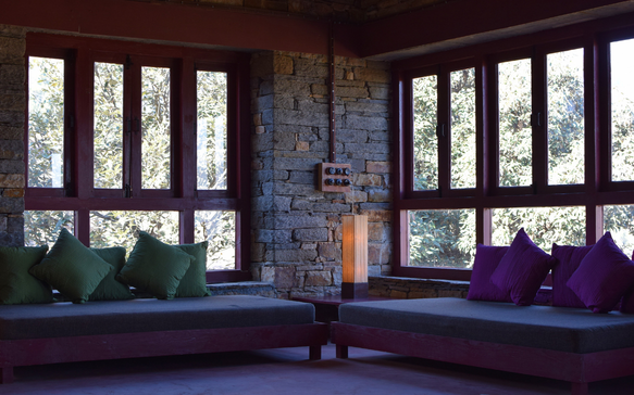 Cozy stone lodge interior with large windows, cushioned seating, and natural light overlooking greenery