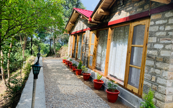 Charming stone cottage with red roof and wooden windows along a garden pathway lined with potted plants