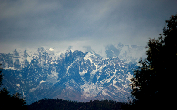 Dramatic snow capped mountain range partially covered by clouds under a moody sky