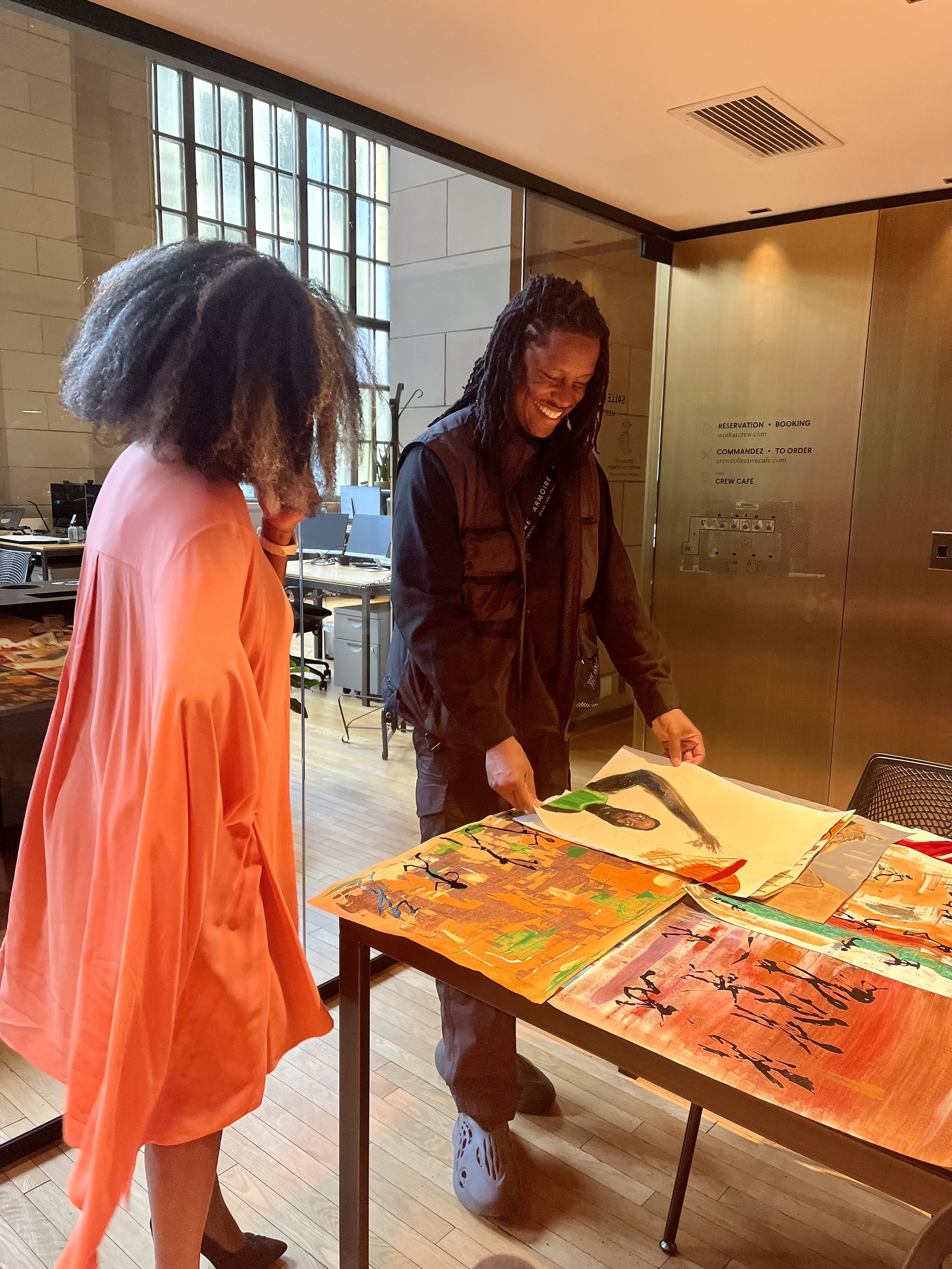 Two people in an office setting looking at colorful abstract artwork spread out on a table.