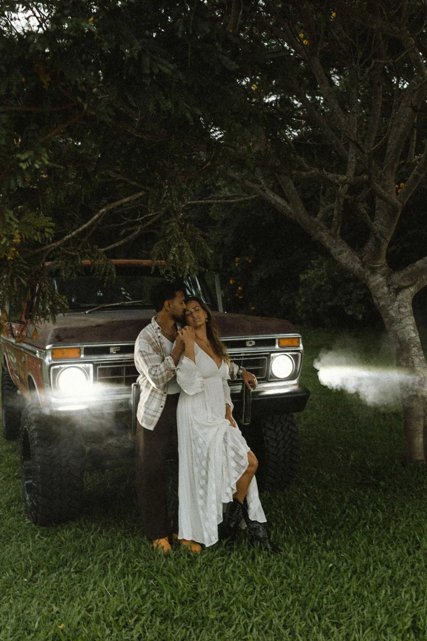 lovers couple at night in front of truck with headlights on and big tree in background