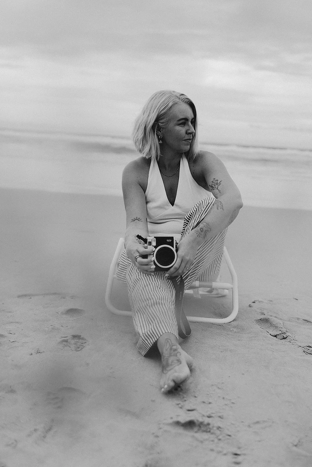 black and white image of photographer on beach holding polaroid camera