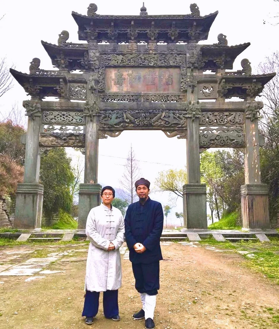 Shifu Chen and Sally Chang at old Wudang Gate with gray winter sky and moss and dirt ground
