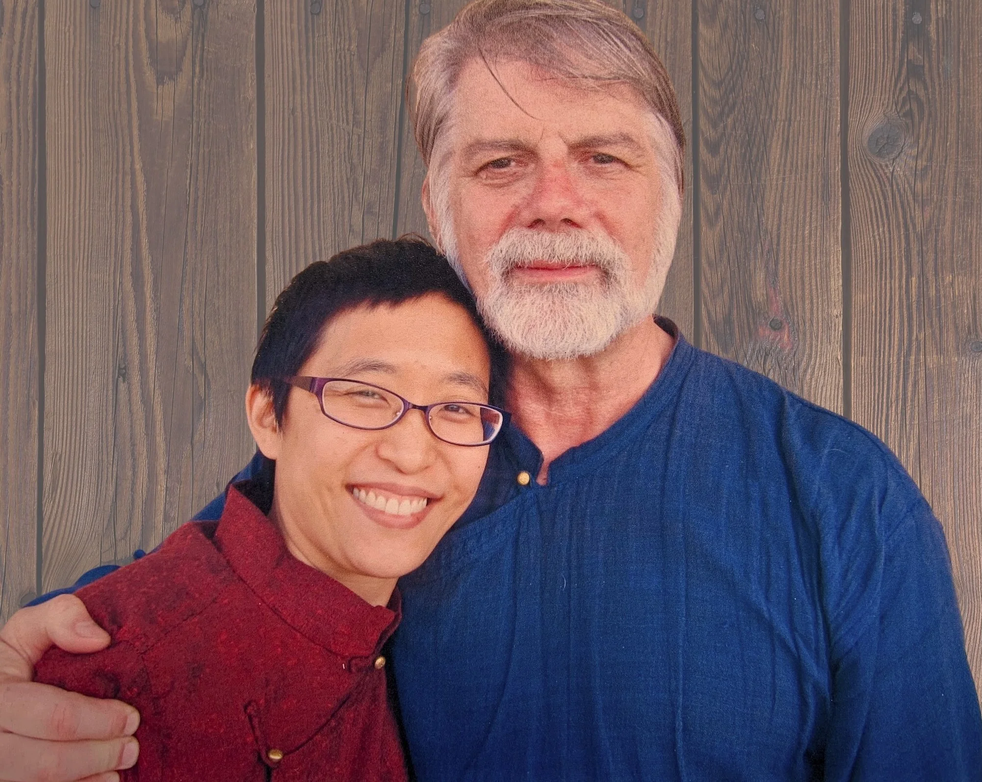 Shifu Ted Mancuso and Sally Chang in blue and burgandy uniform side hug in front of wooden fence