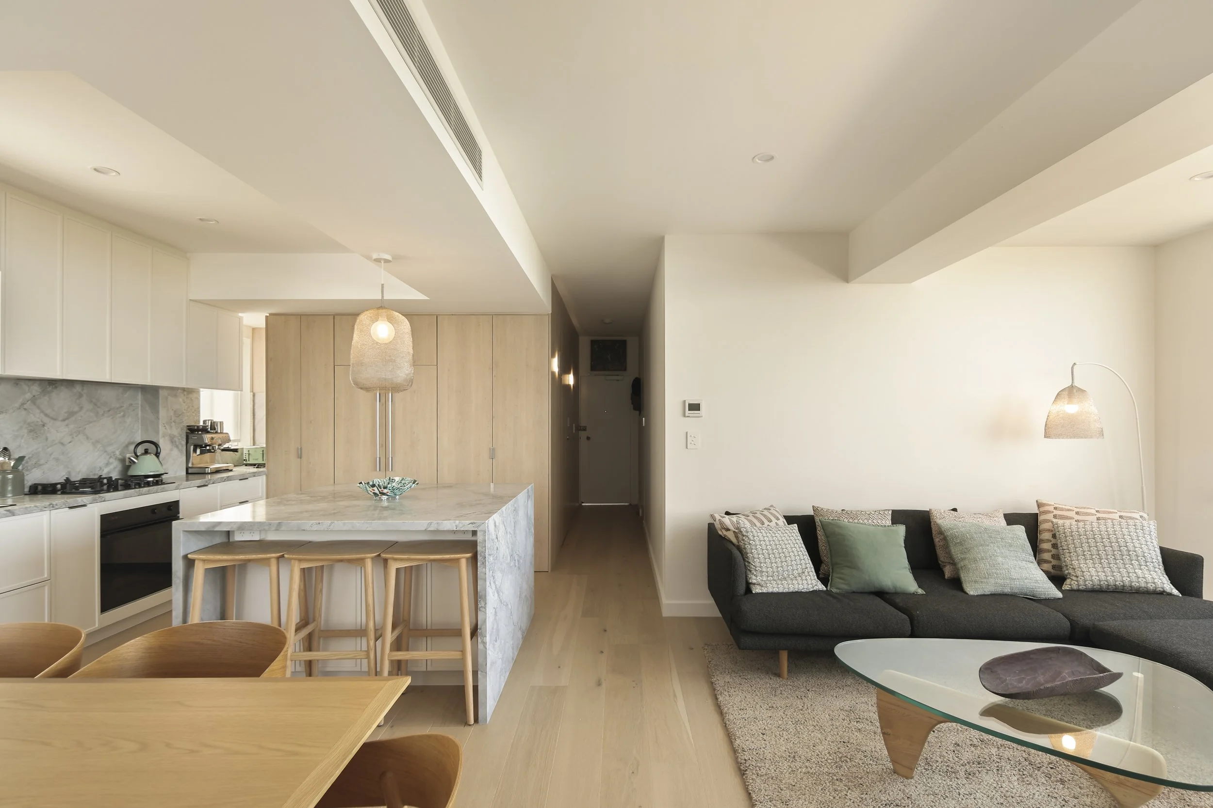 Kitchen and living space with stone benchtops, timber detailing and soft pendant lighting in apartment