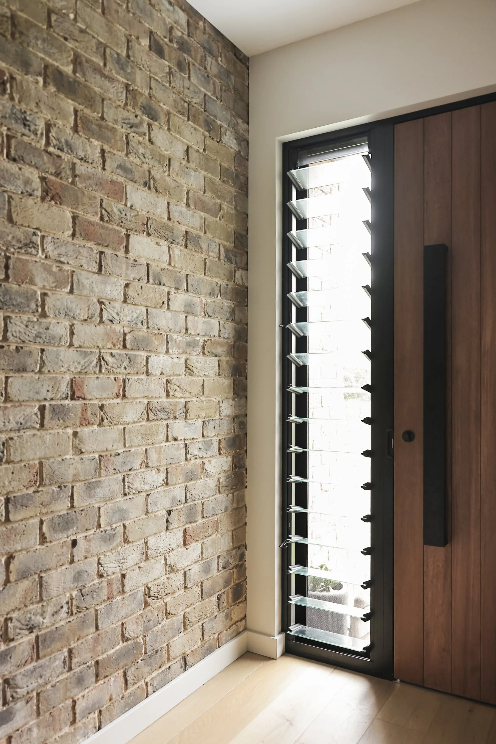 Entry foyer with recycled brick wall, timber front door and louvre window