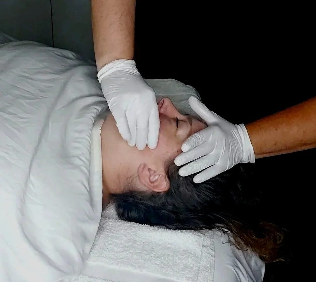 A person receiving a facial treatment from a professional wearing gloves in a clinical setting.