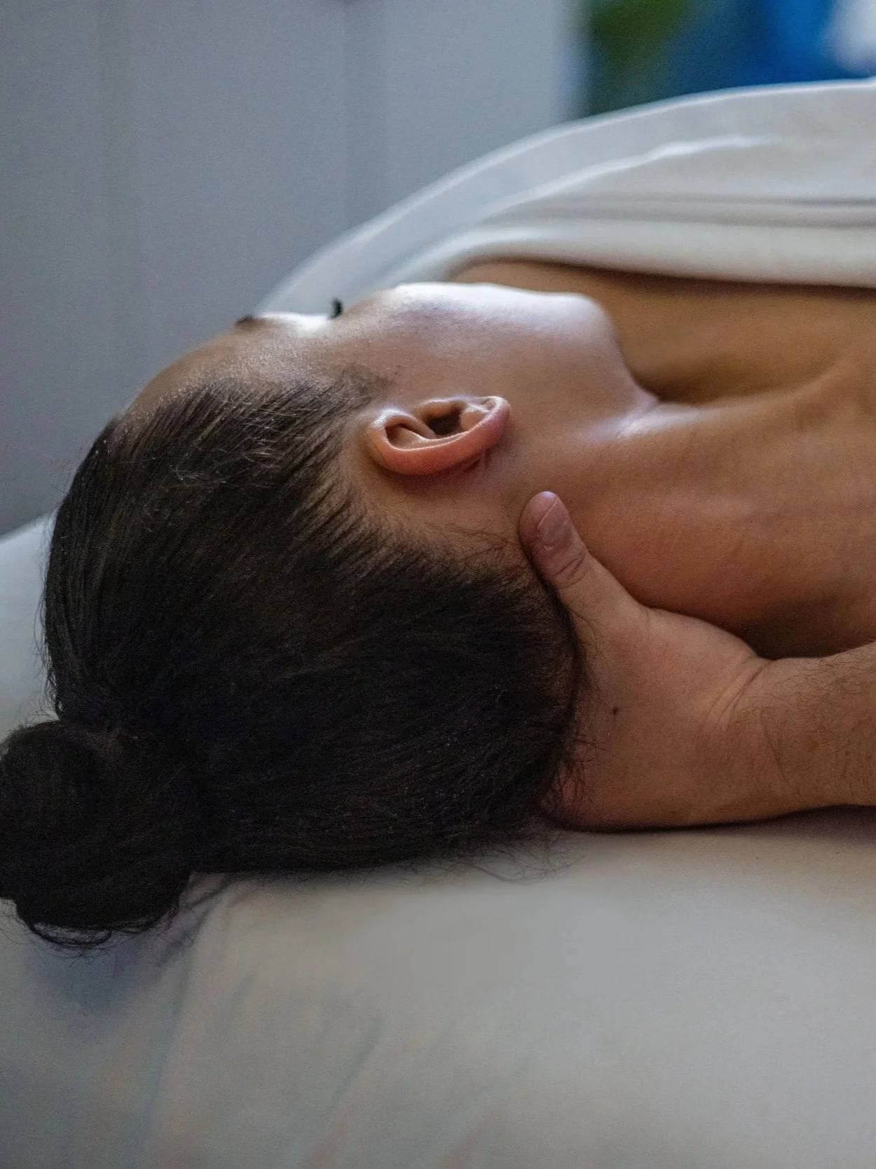 Close-up of a woman receiving a massage, lying face down on a massage table with her hair tied back.