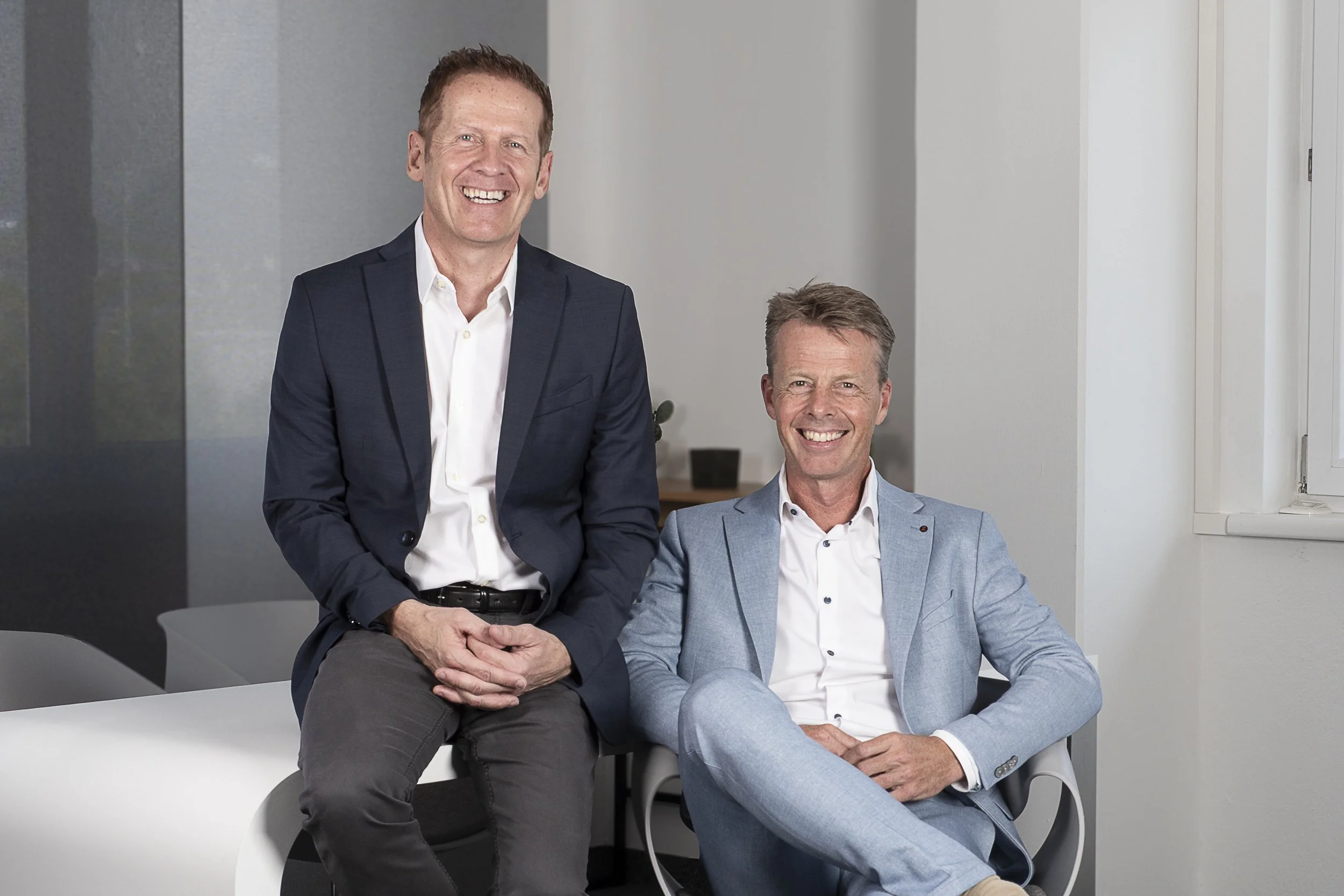 Zwei Männer in Anzügen lachen fröhlich im Büro.