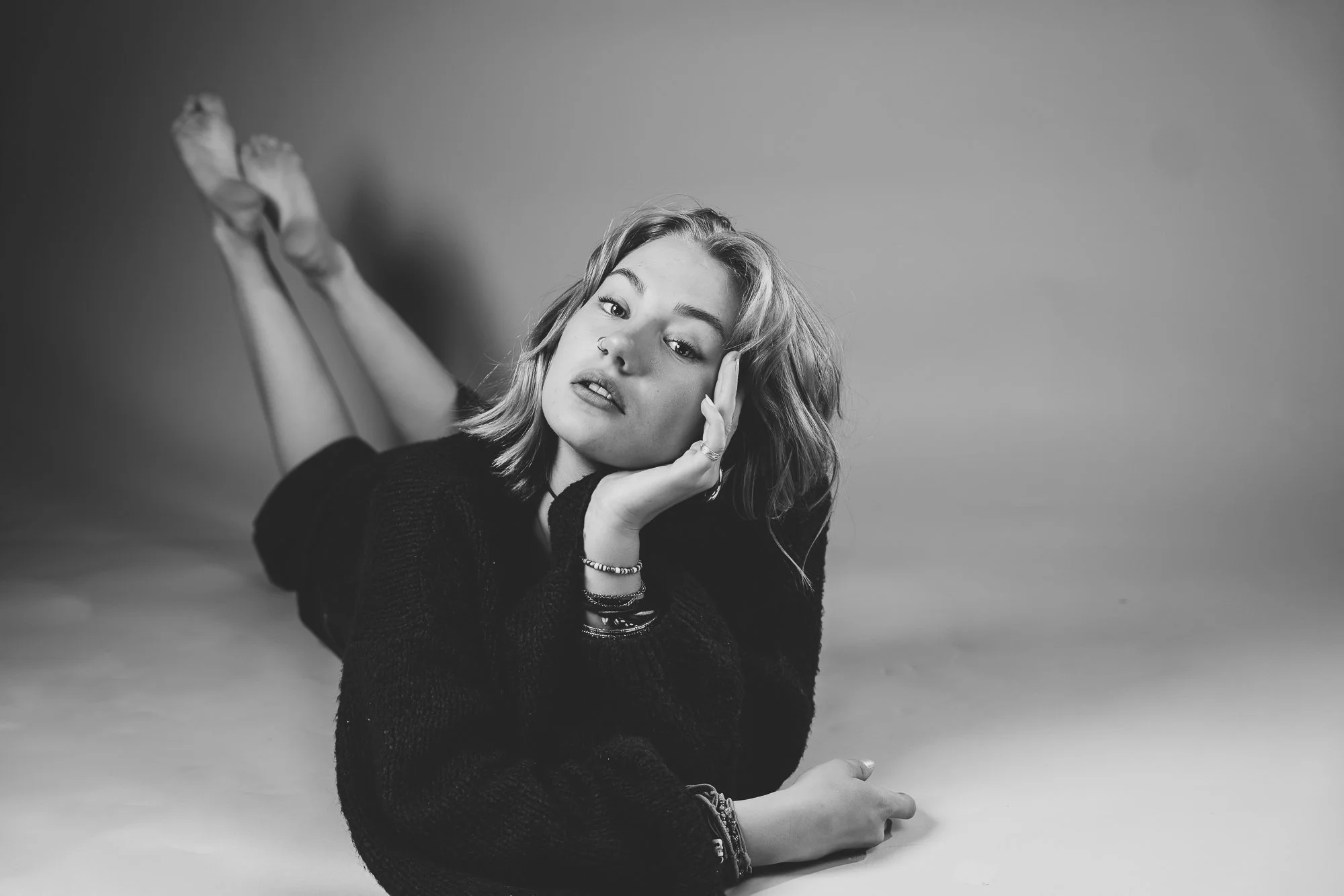 Schwarz-weiß-Foto eines jungen Mädchens, liegend auf dem Bauch, mit Kopf auf der Hand, blickt direkt in die Kamera.