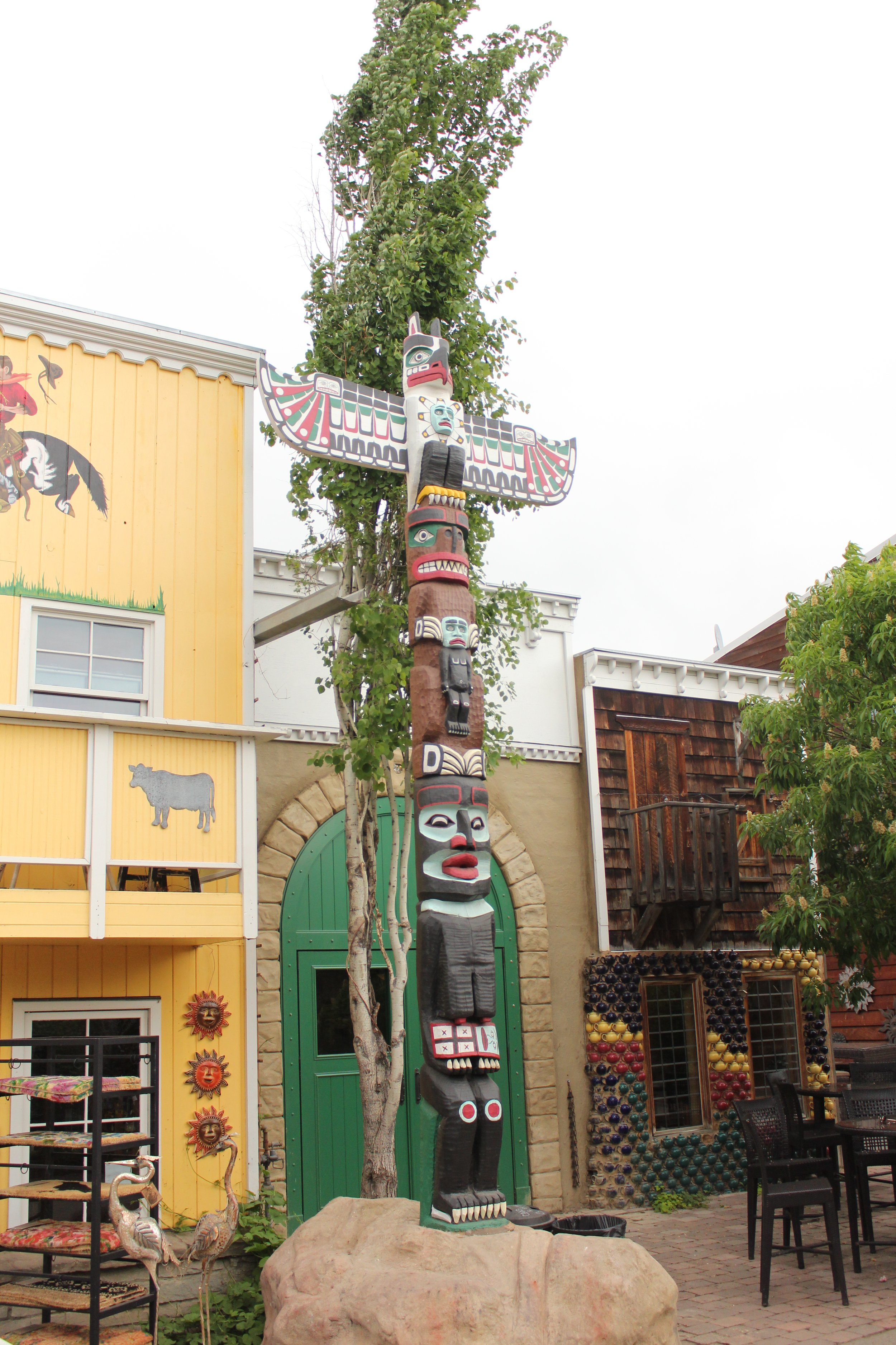 A traditional Native American totem pole painted with colorful faces and symbols, standing outdoors against a cloudy sky with leafless trees in the background.