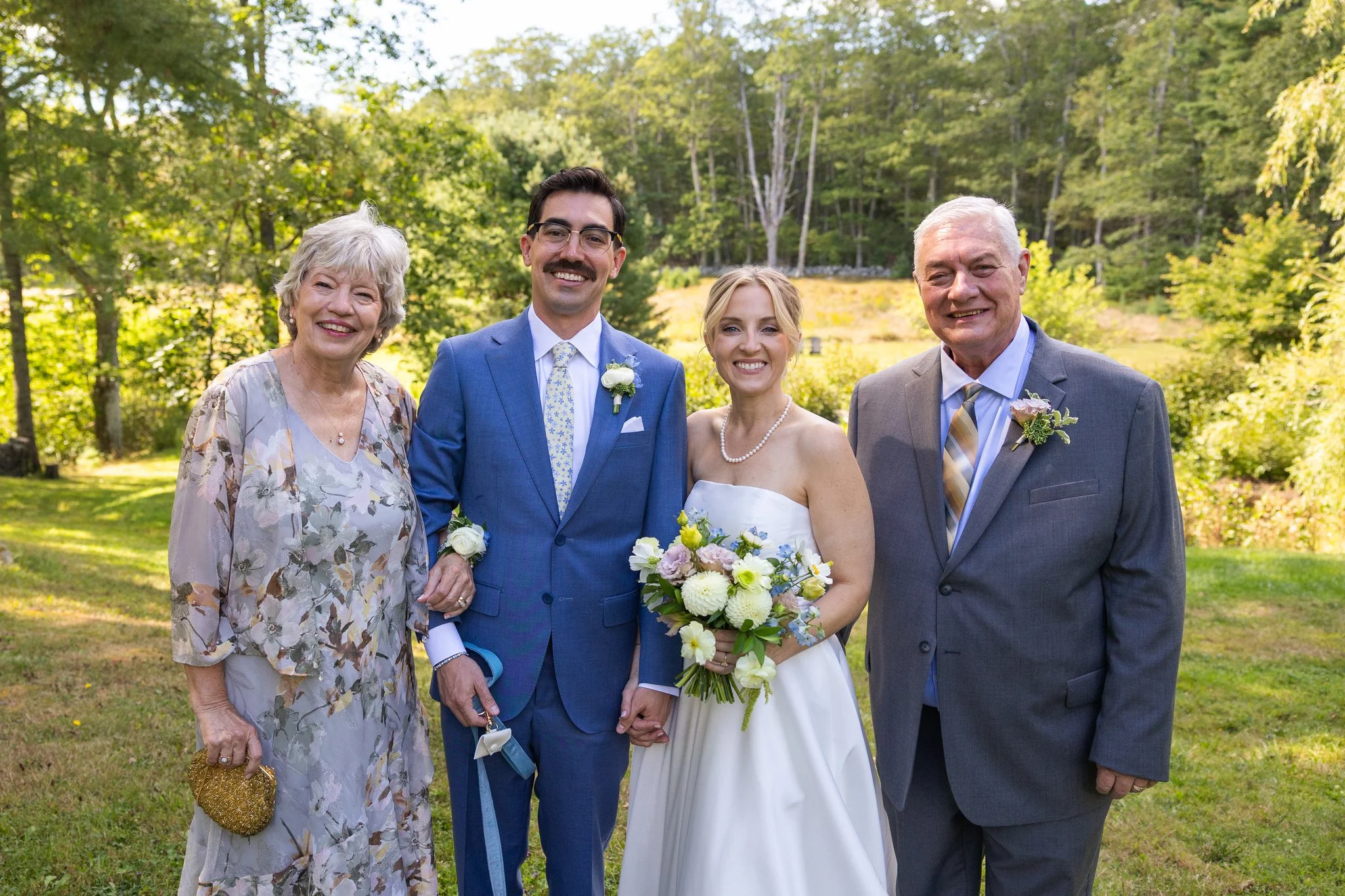 Bride and Groom posing on the lawn at The Squire Tarbox Inn holding wedding flowers designed by Celadon Floral.