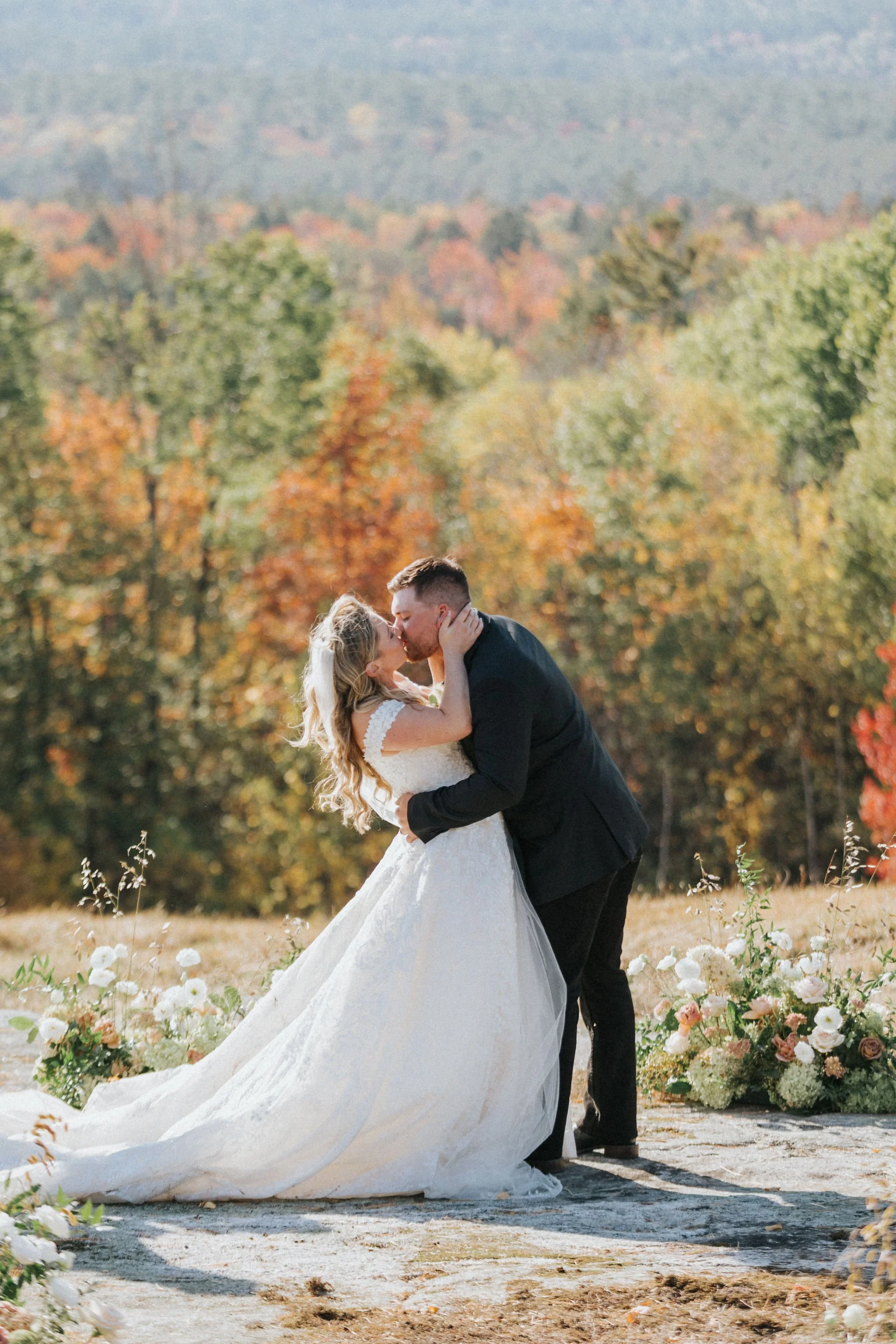 Bride and Groom kiss in the sunlight in a field surrounded by flowers by Maine florist