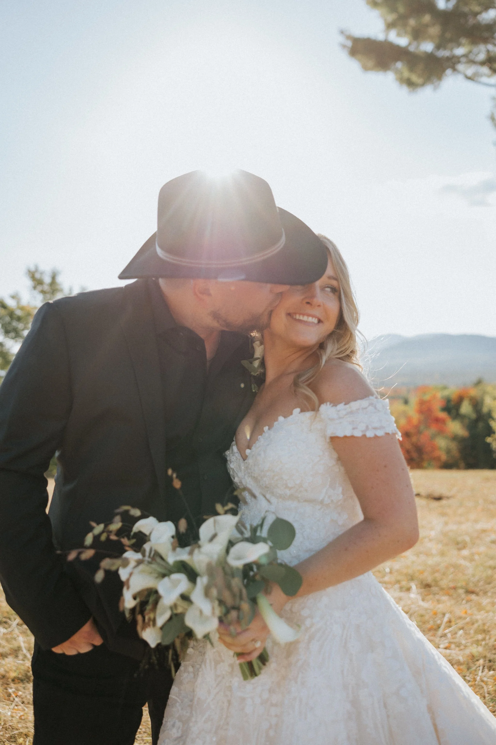 Groom in cowboy hat kisses Bride holding bouquet by Maine florist Celadon Floral