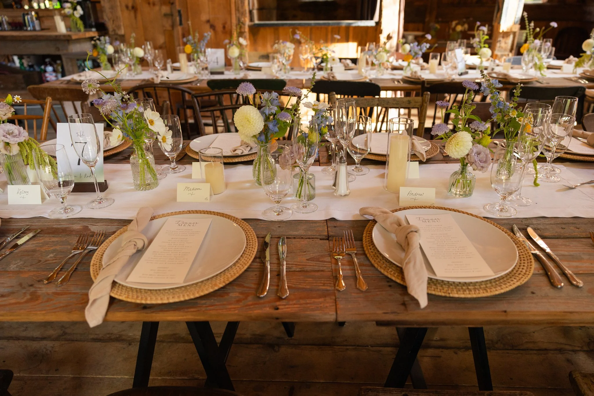 Close up of small bud vases with pale blue, lavender, white, and gold flowers arranged by Celadon Floral for a Maine wedding