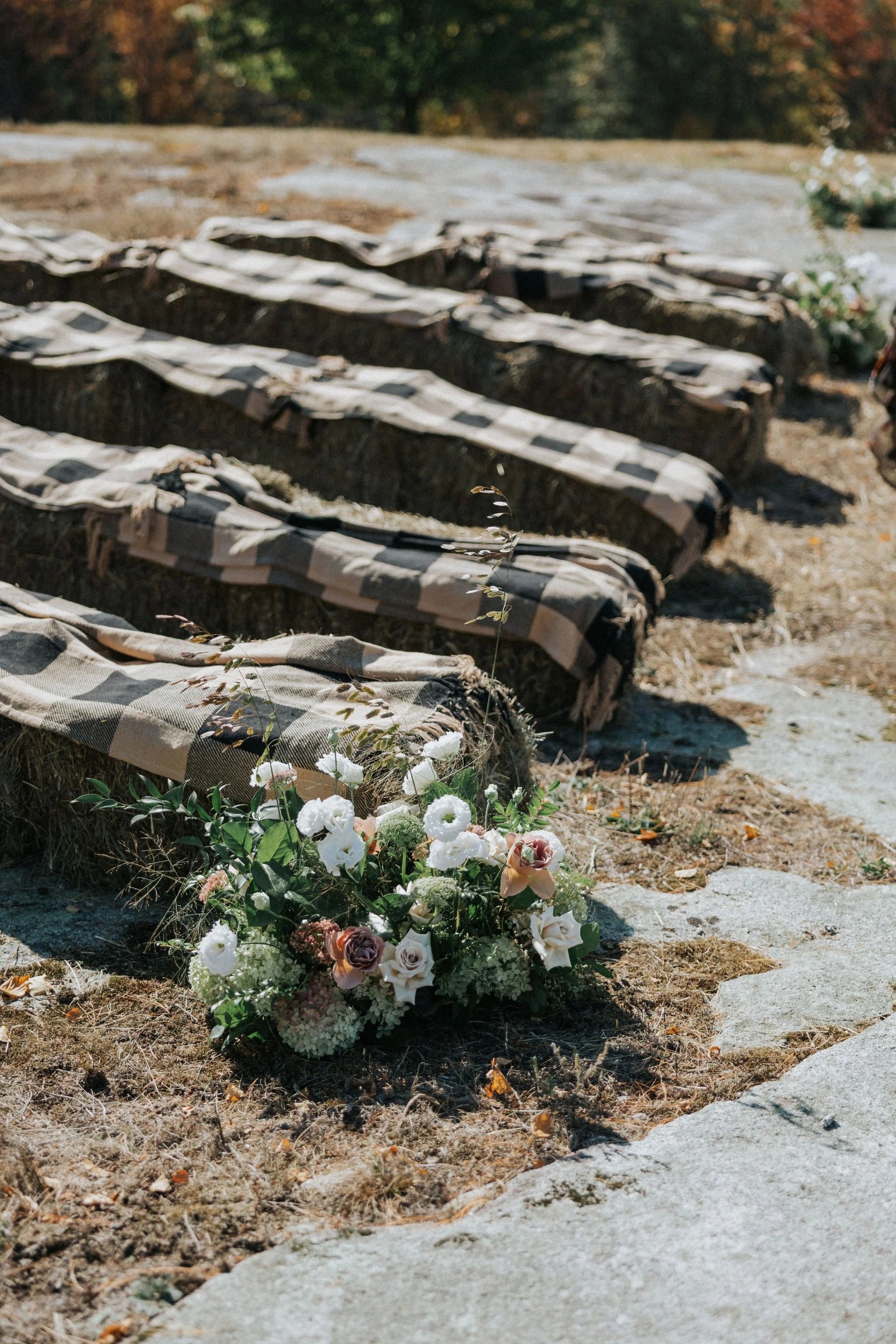 Beautiful grounded flowers by Celadon Floral in front of hay bales at rustic Maine wedding ceremony.