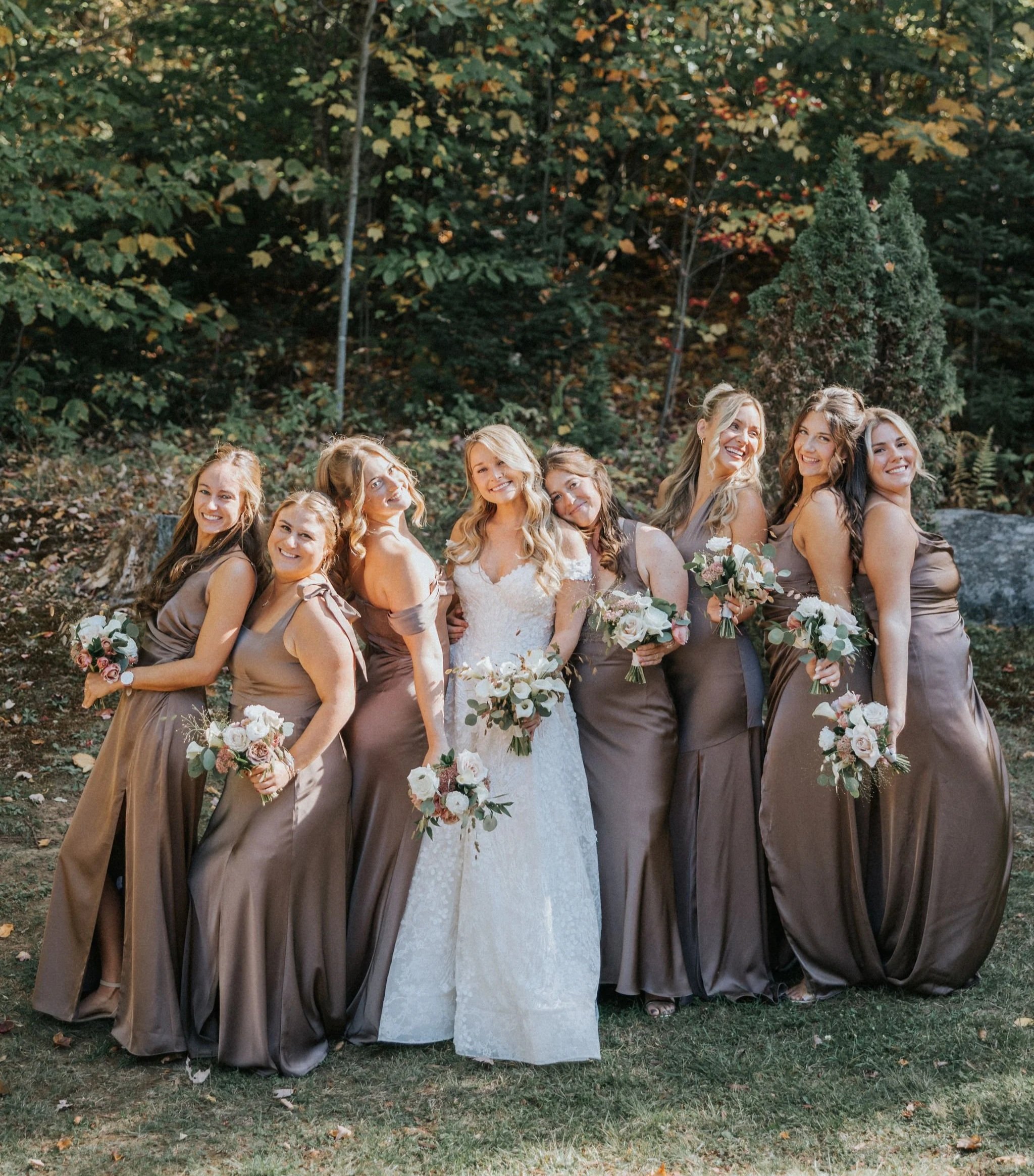 Bride in white dress posing with bridesmaids in toffee dresses holding white bouquets at a Maine wedding arranged by Celadon Floral