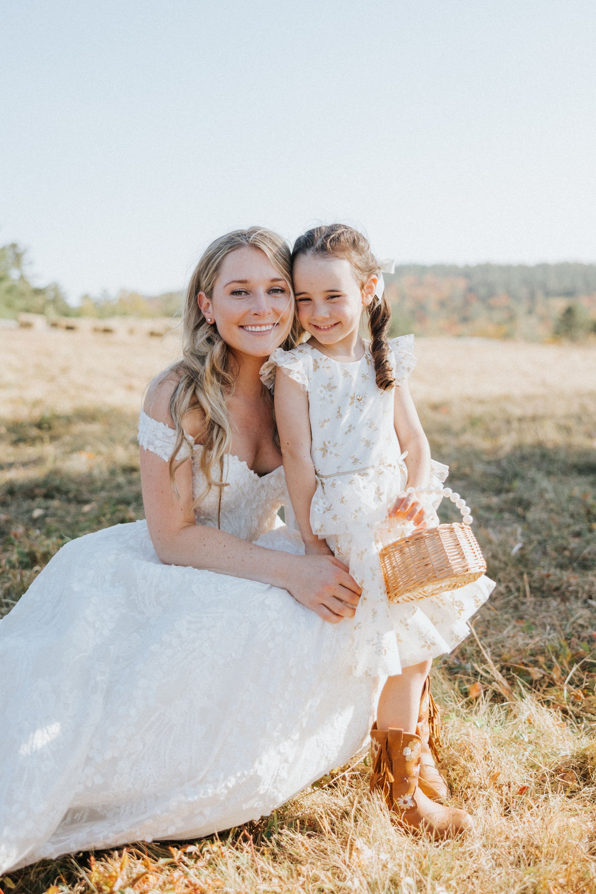 Smiling flower girl poses with Bethel, Maine bride in the sunlight.