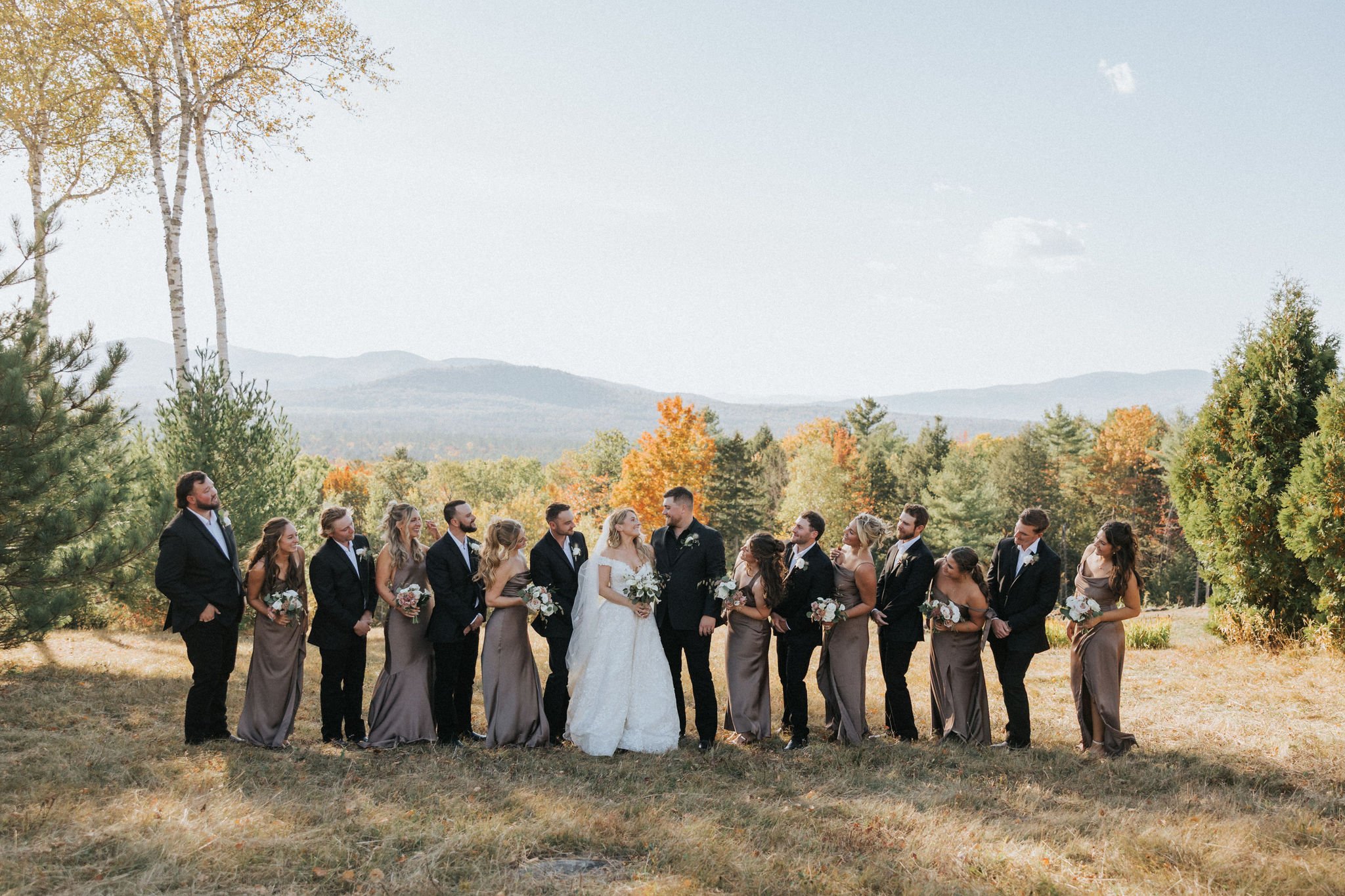 Newlyweds and wedding party pose in an open field holding white bouquets by Celadon Floral