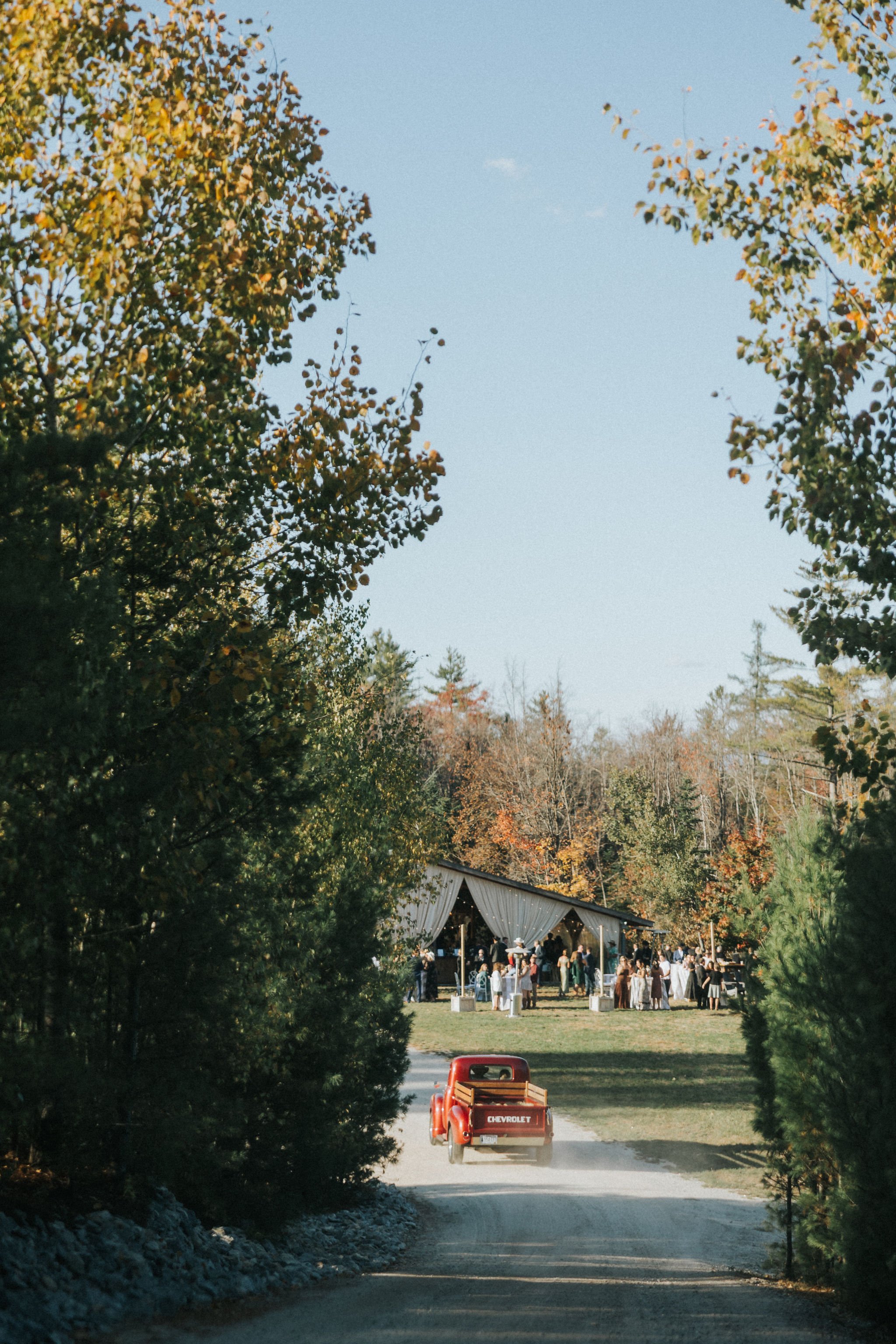 Cherry red Chevrolet driving down dirt road to Maine wedding reception