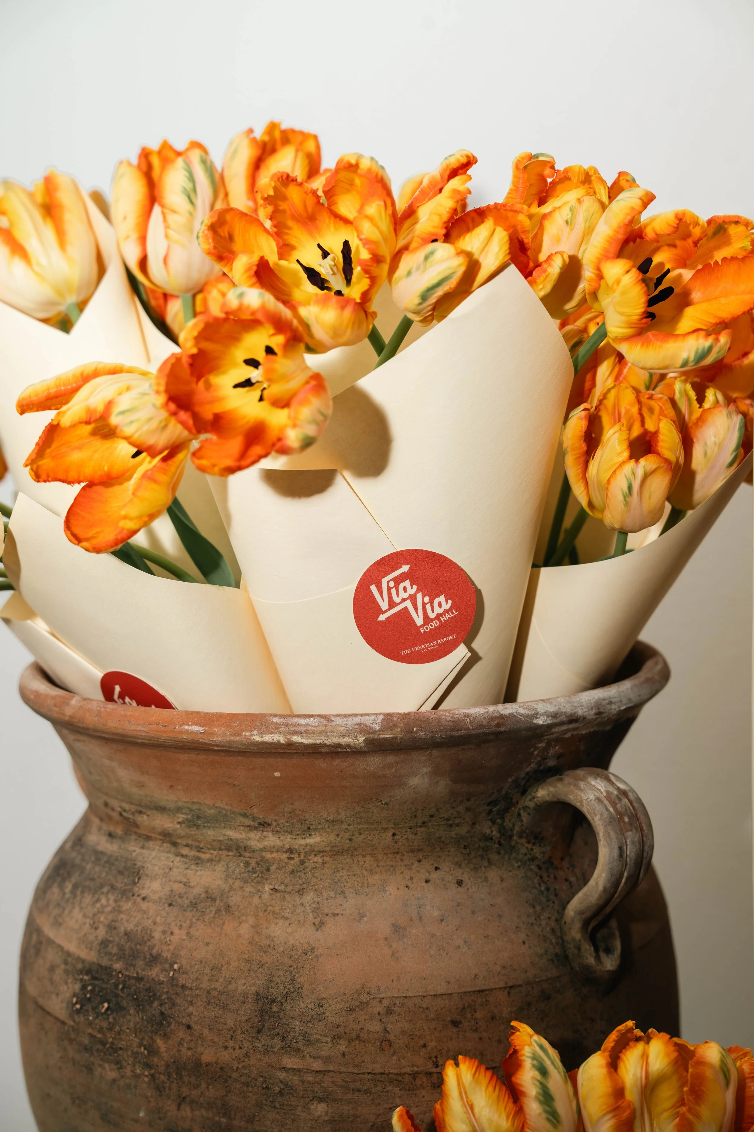 Bright orange and yellow tulips in paper wraps inside an old terracotta vase.