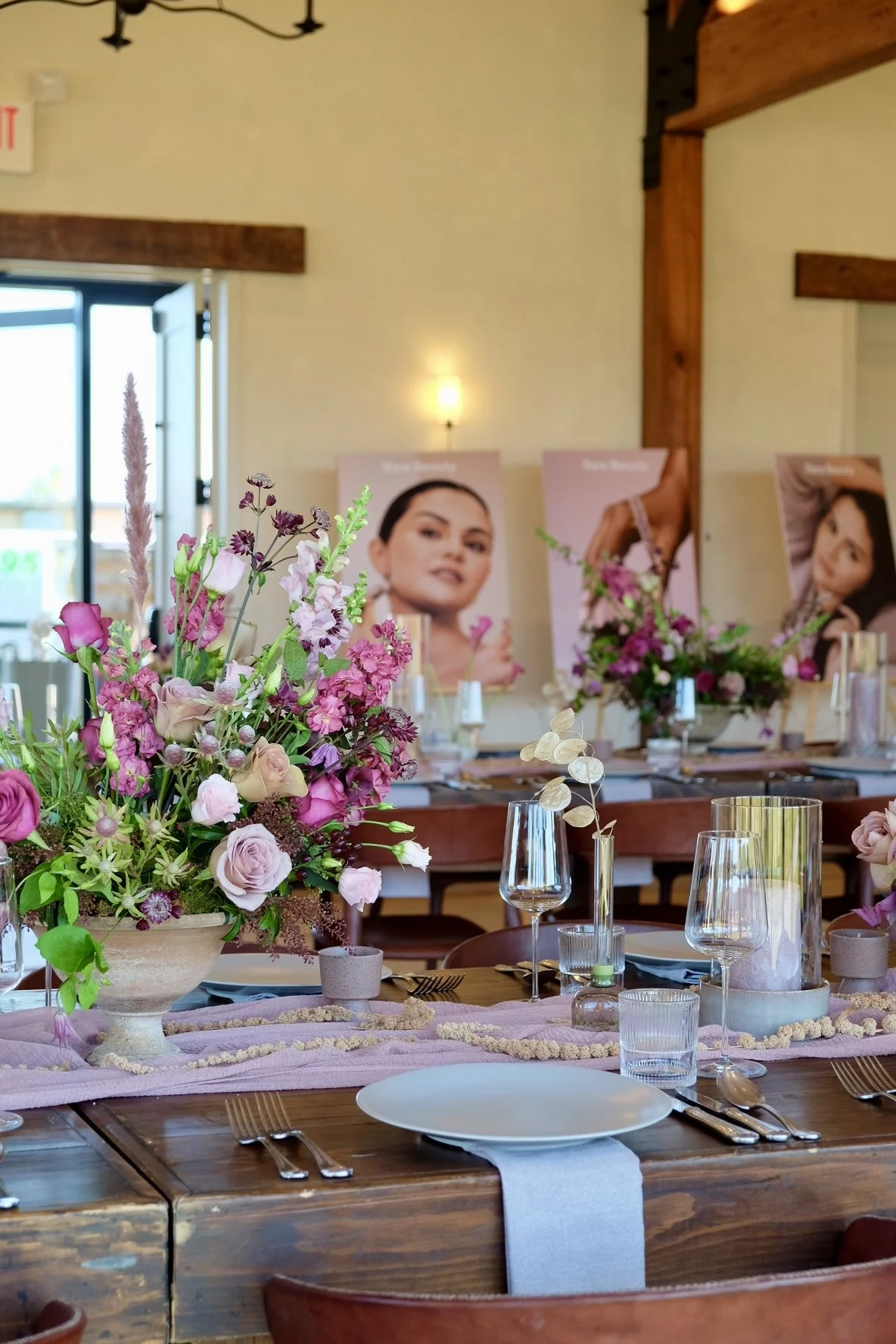 Elegant banquet table decorated with pink and purple flowers, glassware, and table settings, with promotional posters in the background.