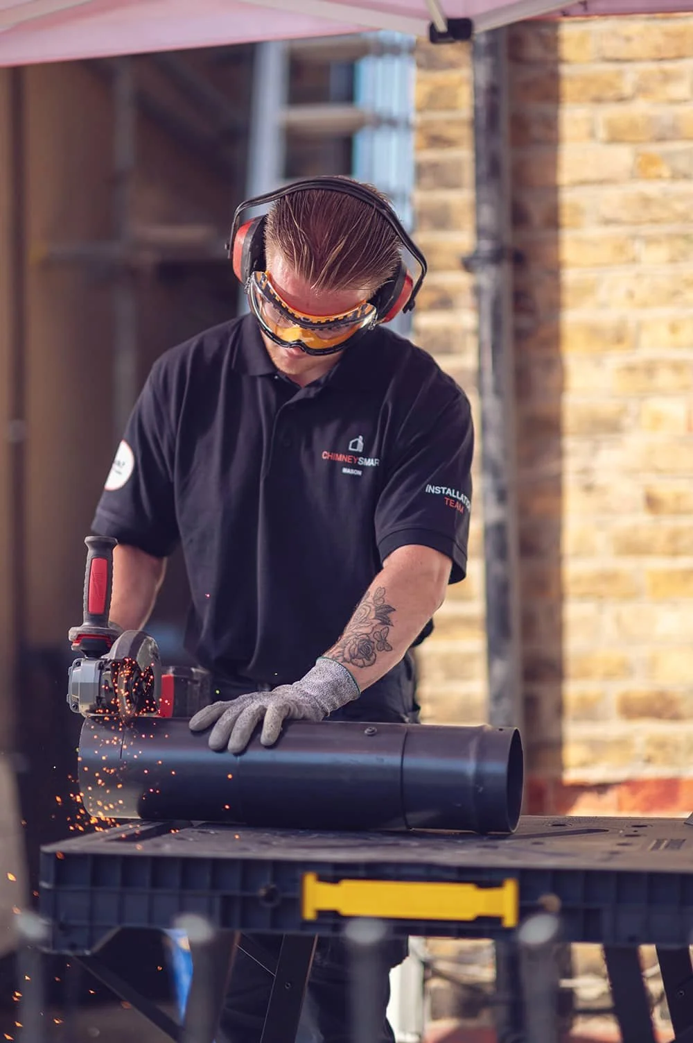 Chimney Installation team member sawing metal pipe creating sparks of company ChimneySmart in North London