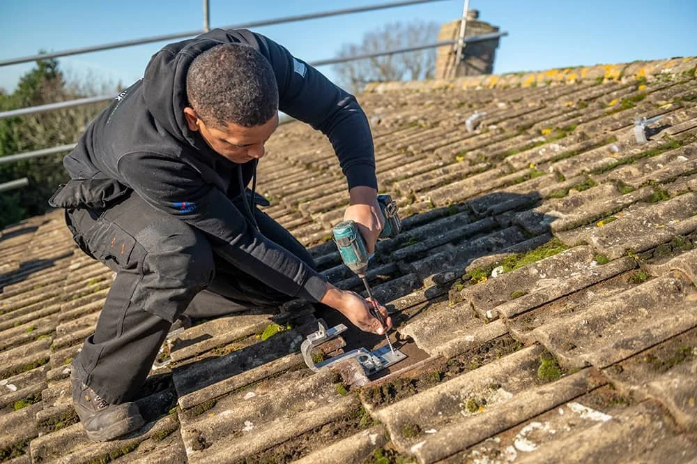 Electrical engineer on the roof drilling tiles ready for solar panel installation at Lumisol electrical company in Norfolk