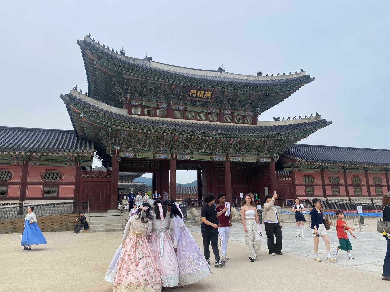 A beautiful traditional building in South Korea, surrounded by tourists and young women in traditional Korean dress.