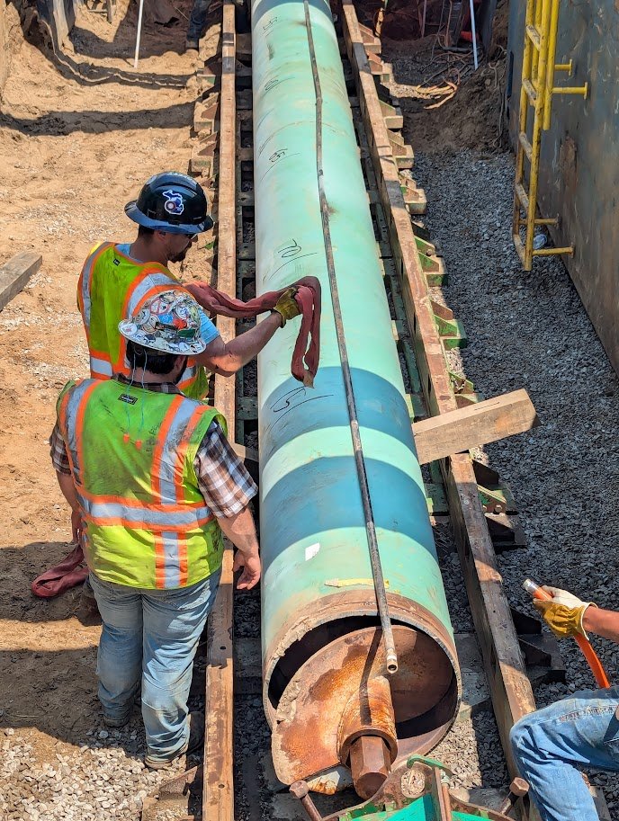 Workers preparing pipeline section for installation using auger bore method in construction site