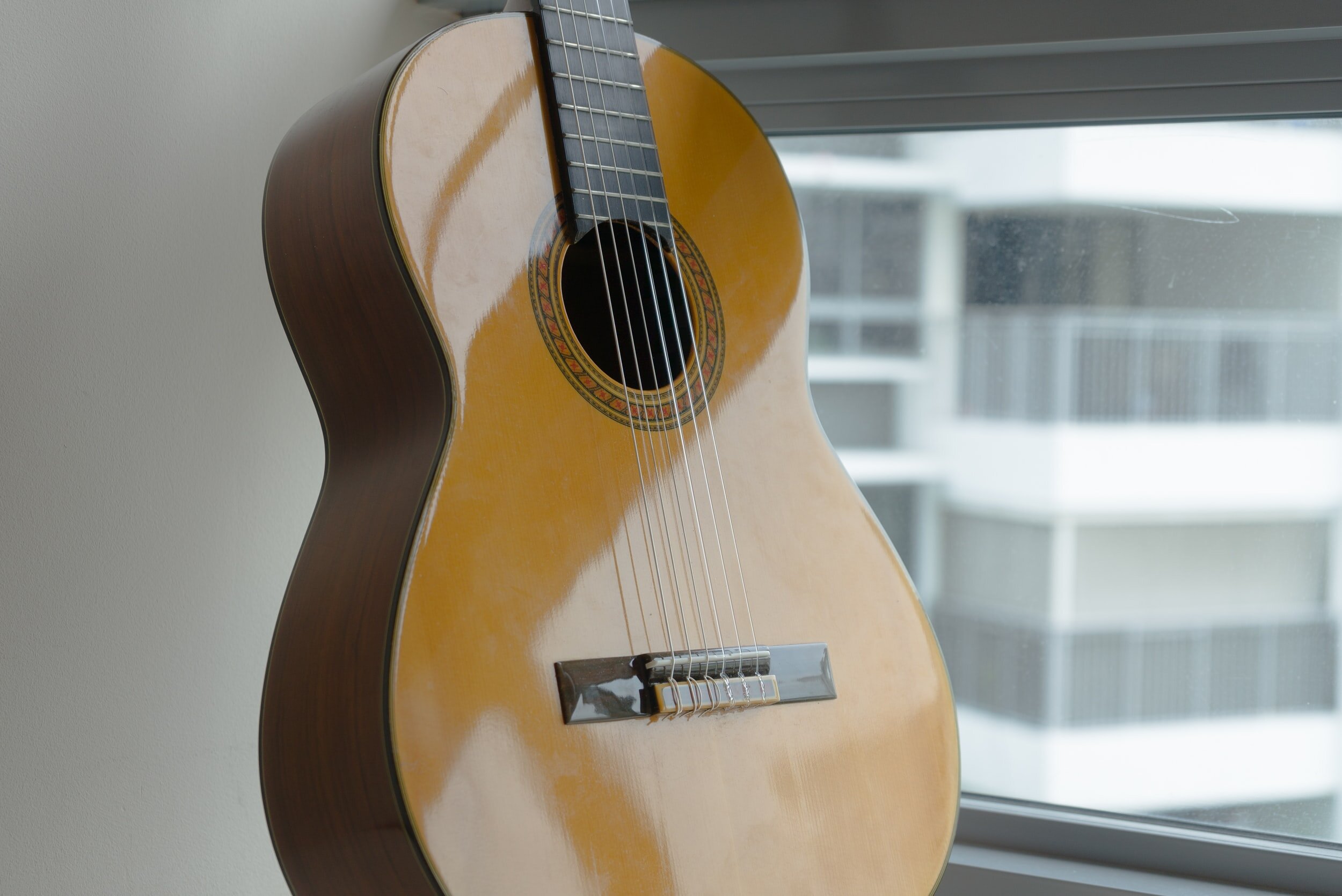 An acoustic guitar leaning against a wall near a window.
