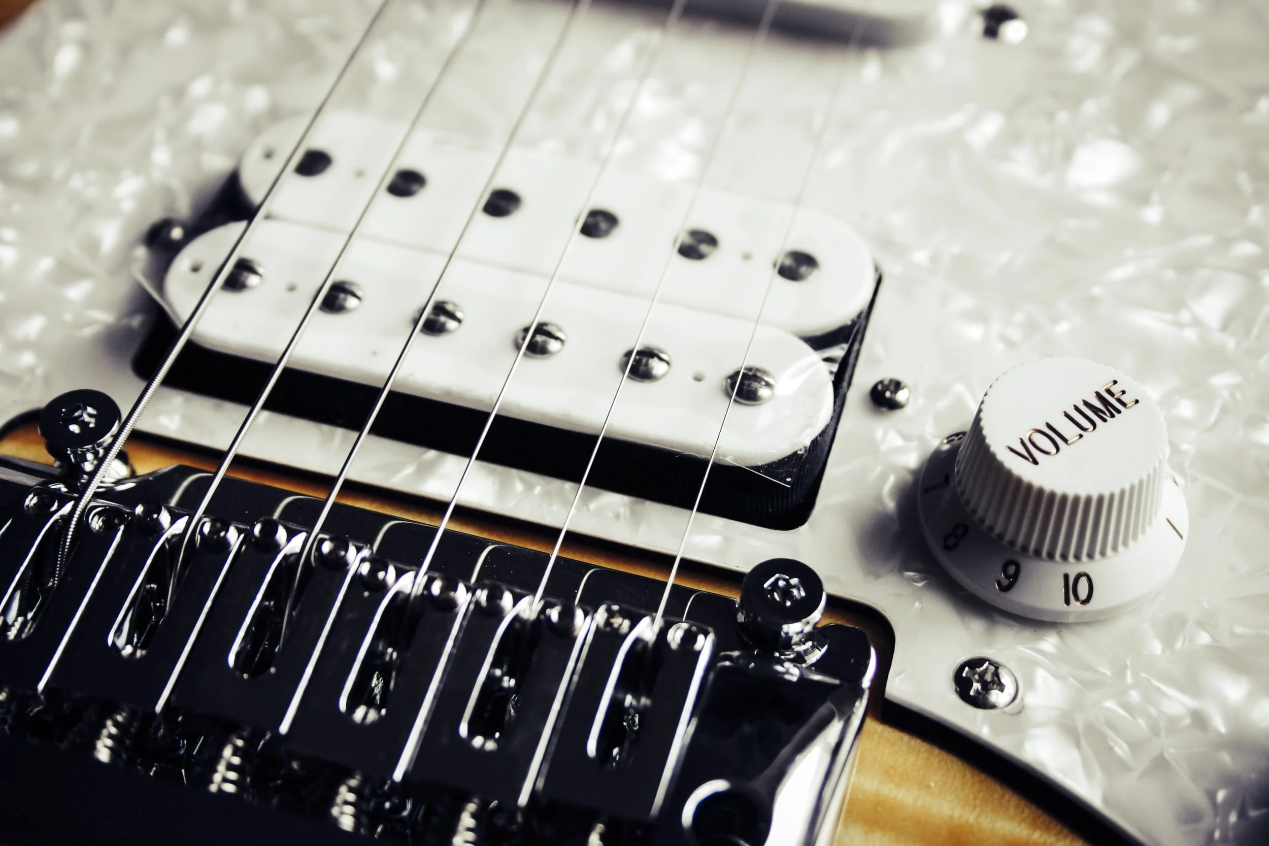 Close-up of an electric guitar bridge, pickup, volume knob, and strings, with a textured white background.
