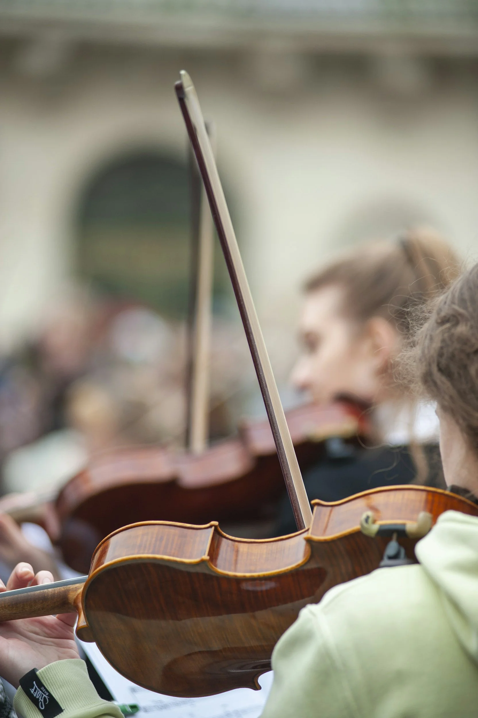 A close-up of string instruments, likely violins, being played by a group of musicians during a performance or practice.