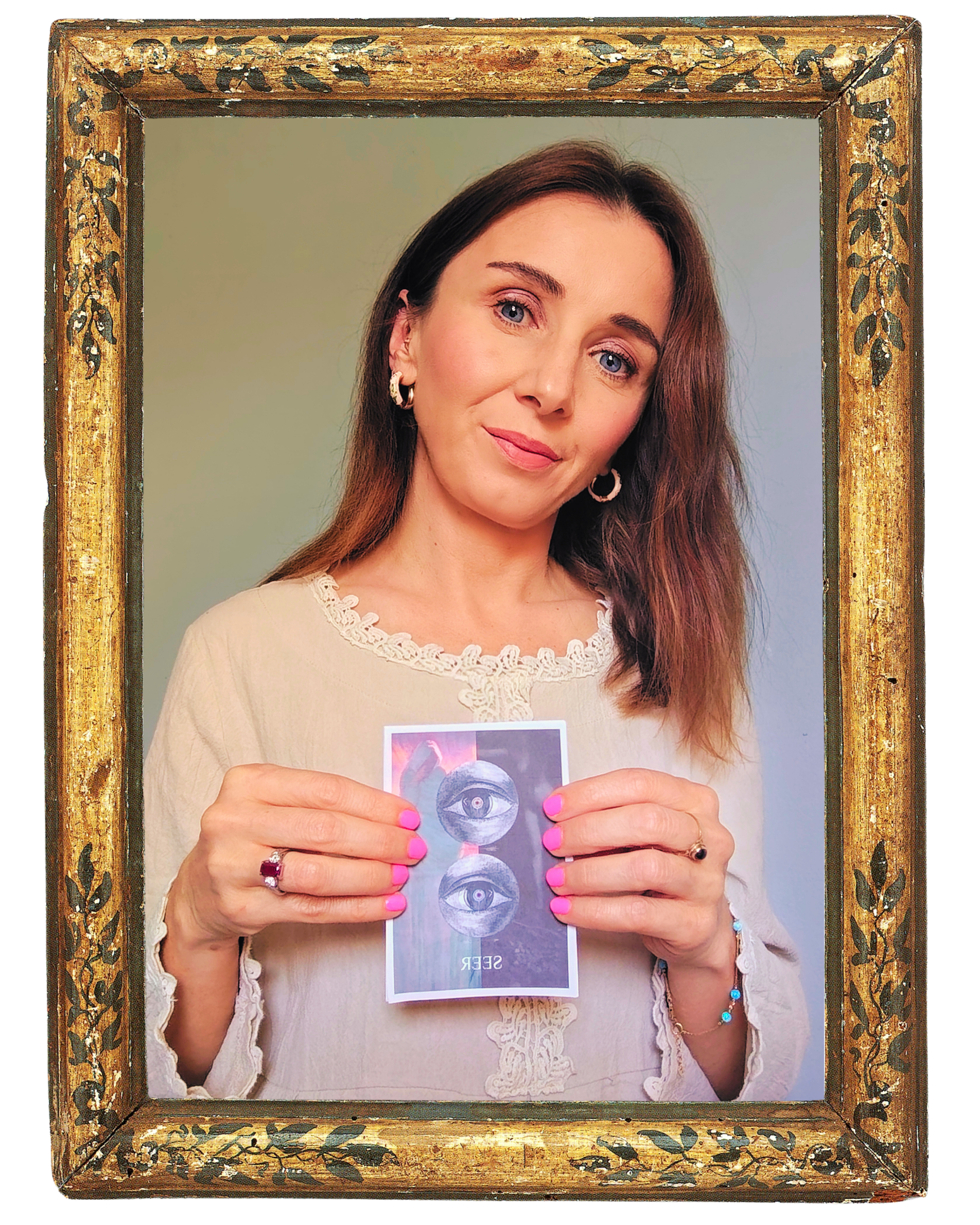 A woman with long brown hair and blue eyes holding a card with multiple eye illustrations in front of her chest. The woman is wearing hoop earrings, a ring with a dark stone, and a bracelet with turquoise beads. She is inside a gold-colored decorative picture frame with black floral designs.