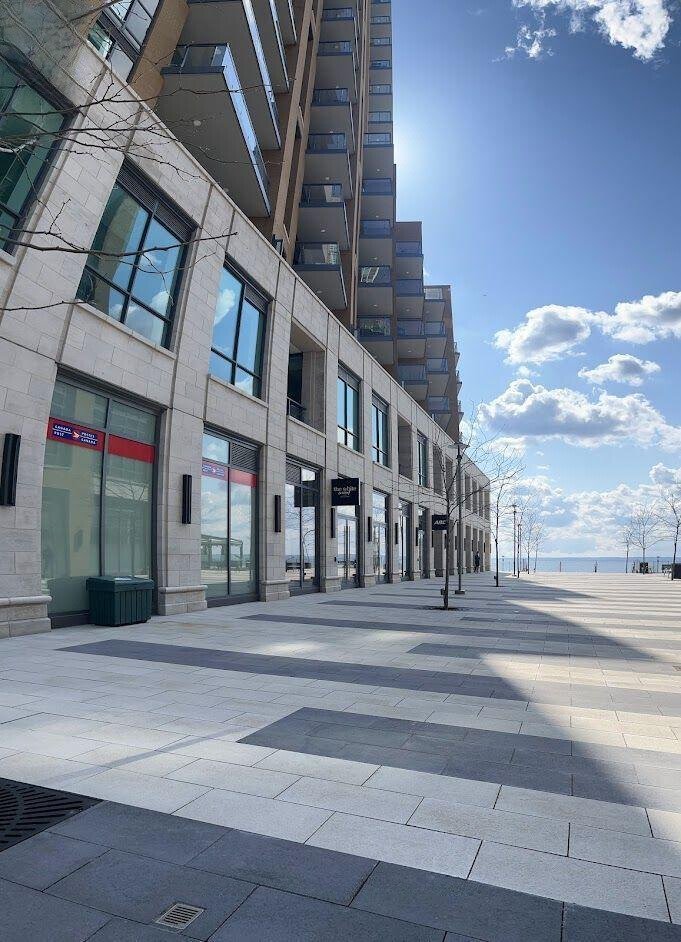 Modern urban building with large windows and balconies, adjacent to a wide, open plaza with a clear sky in the background.