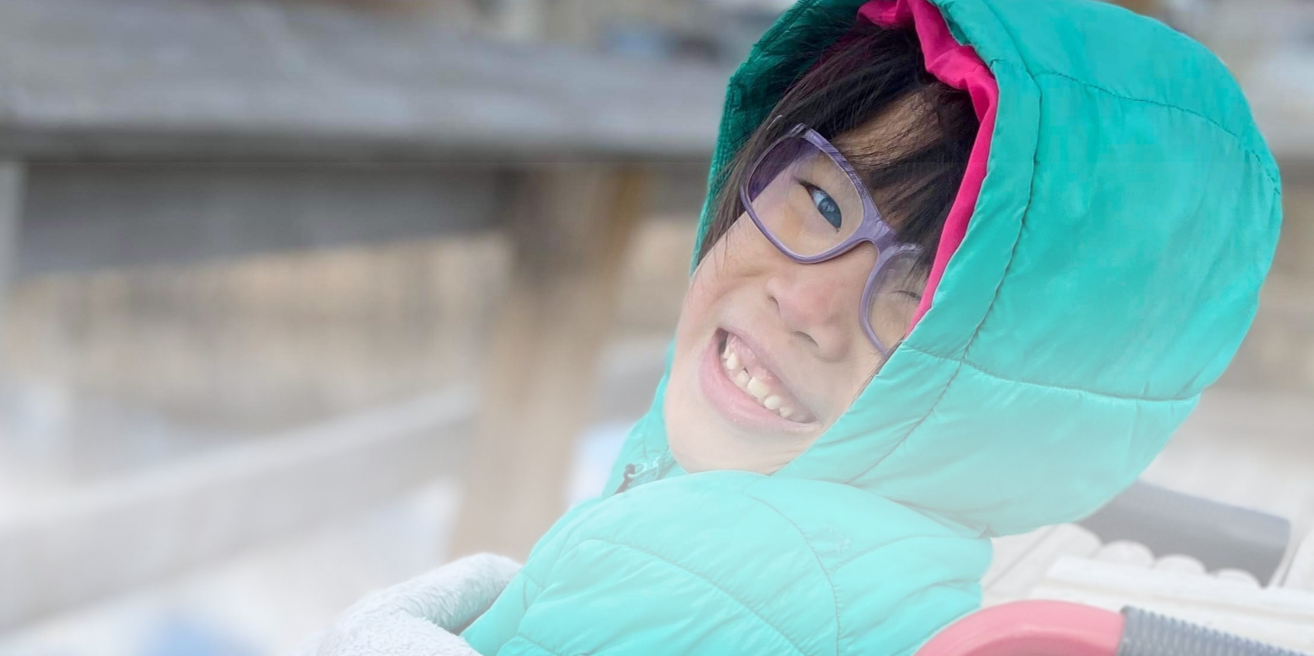 Close-up of a smiling woman wearing glasses and a colorful hooded jacket outdoors.