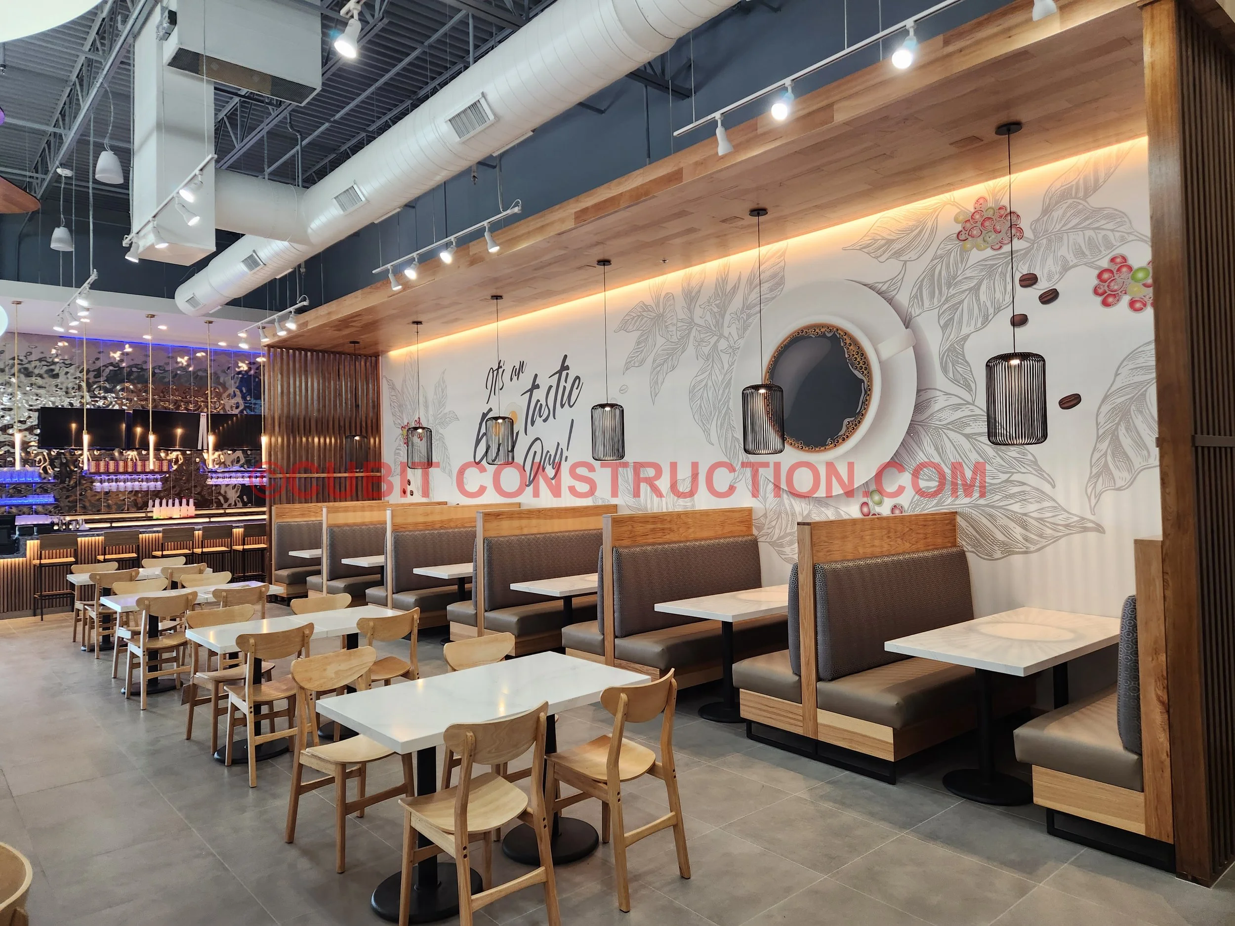 Cafe interior with wooden booths and chairs, white tables, wall mural with coffee cup and coffee beans, and decorative pendant lights