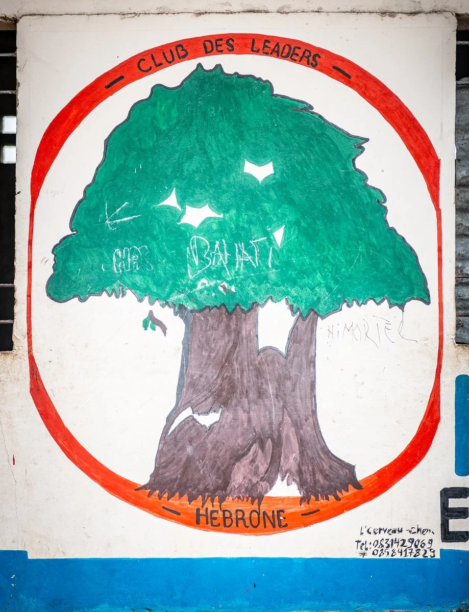 Street art of a large tree with green leaves and a brown trunk, enclosed in a red circle. The words 'Club des Leaders' are written at the top in red, and 'Hebdome' at the bottom. There is a small white graffiti message on the tree's leaves and some handwritten text in the bottom right corner.