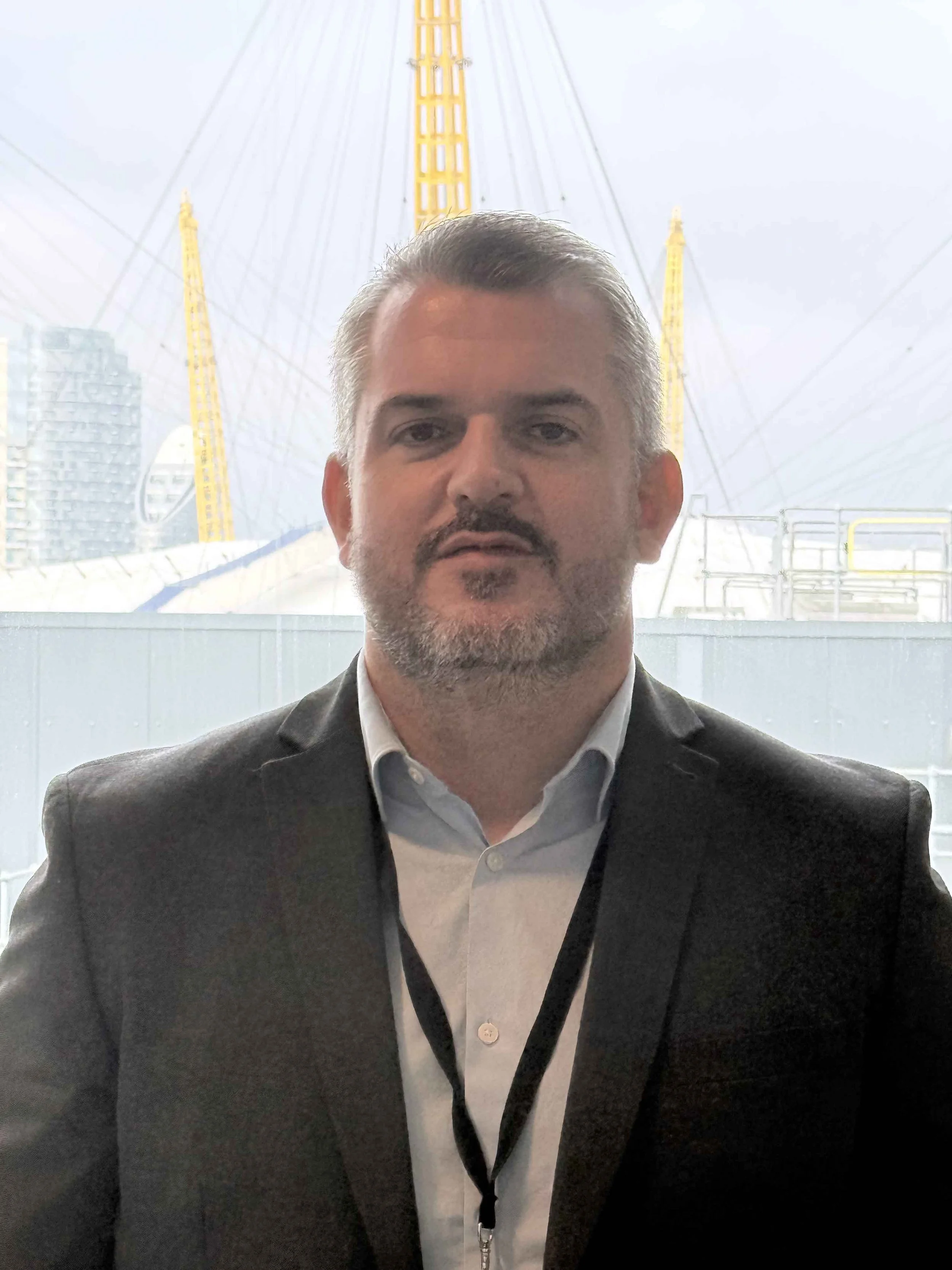 A young man with light brown hair and wearing a white shirt, standing in front of a cityscape with skyscrapers and cranes.
