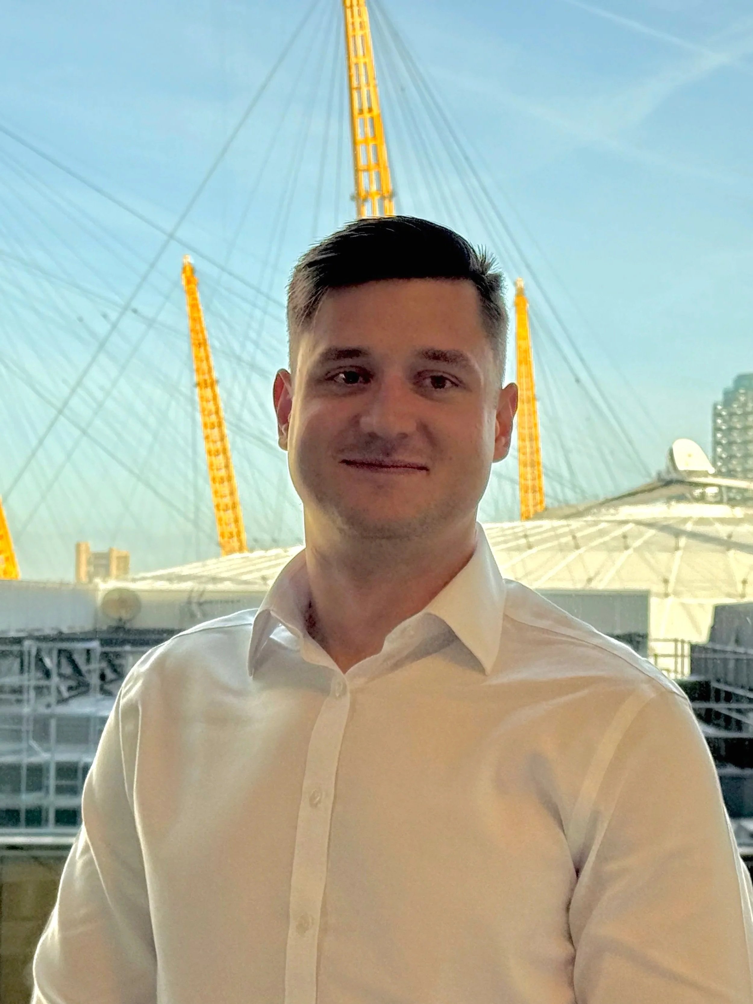 A man in a white dress shirt standing in front of a large Ferris wheel at an amusement park during the daytime.