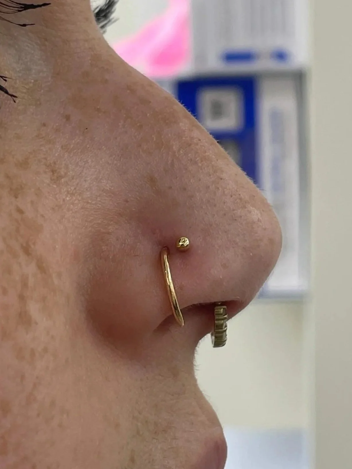 Close-up of a person's face, showing a nose with a gold nose ring and a smaller ring on the nostril septum, as well as eye makeup with long, dark eyelashes.