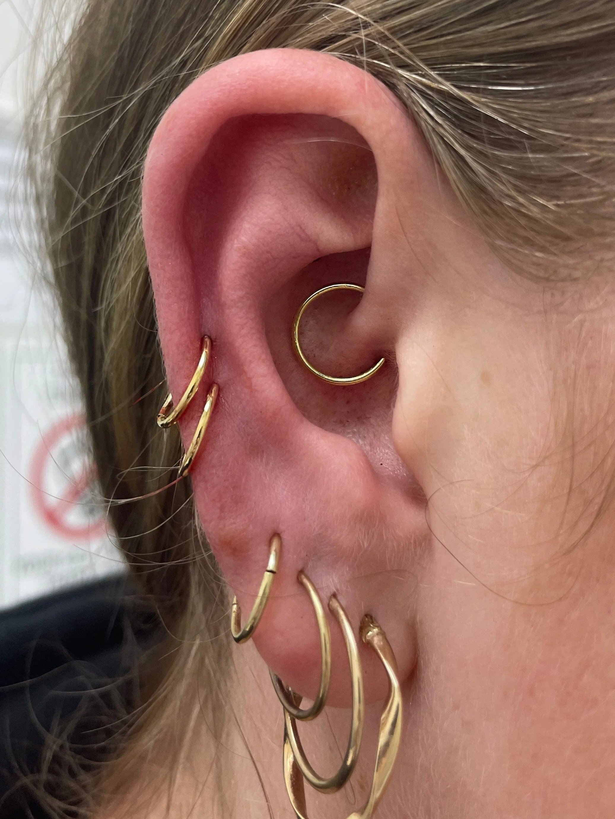 Close-up of a person's ear decorated with multiple gold earrings, including a hoop in the helix and several other hoops along the earlobe.