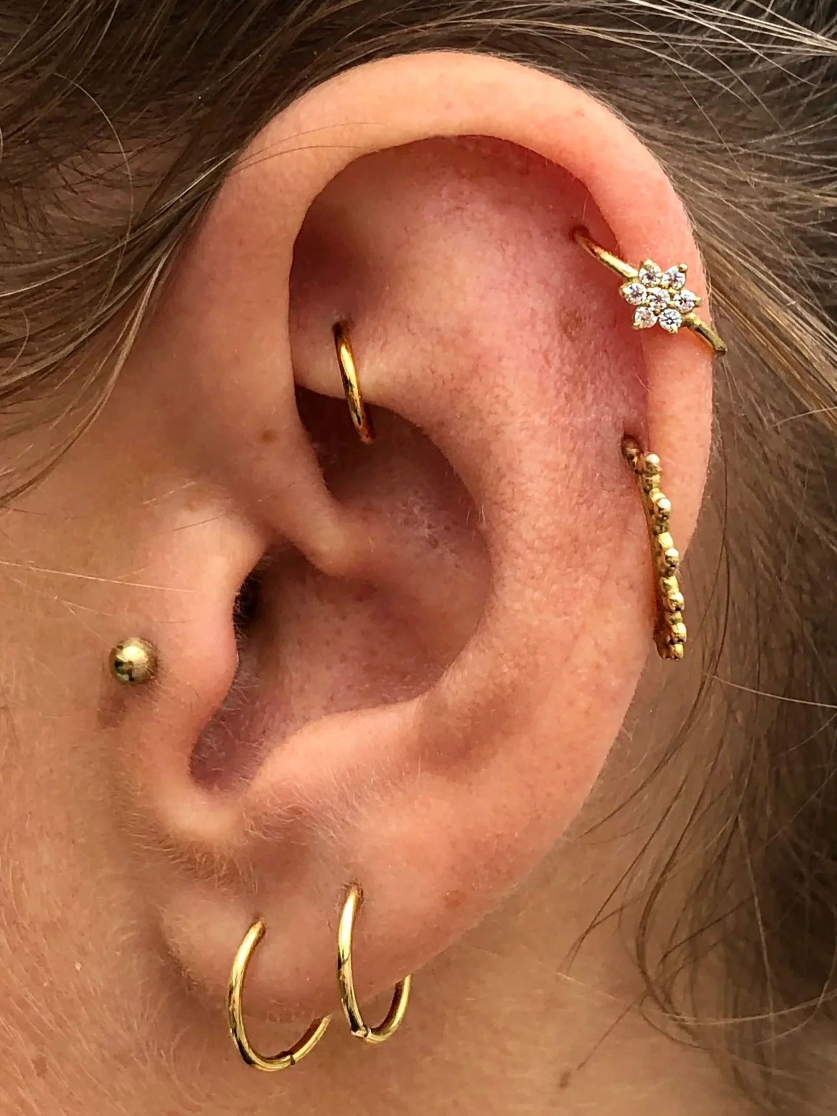 Close-up of a person's ear with multiple gold and diamond piercings, including hoops and a stud.
