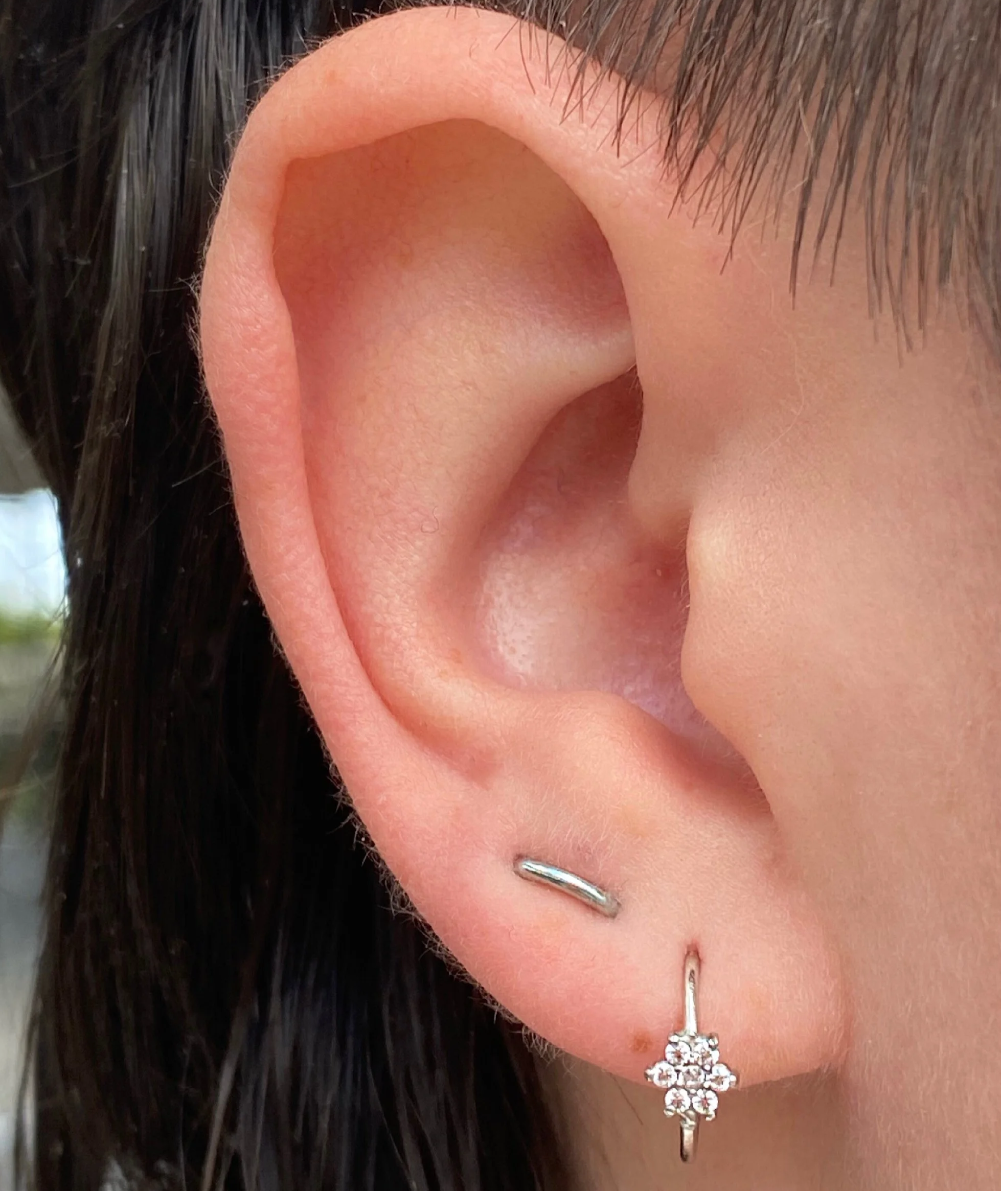 Close-up of a person's ear with two earrings: one small silver hoop and a small diamond flower-shaped stud.